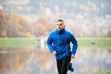 Athlete at the lake running against colorful autumn nature