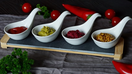 Sauces for meat in stock pesto, sauce French mustard, horseradish, ketchup in white saucers on a stand in dark background