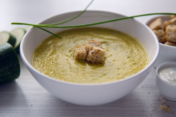 zucchini soup on a white wooden table with croutons