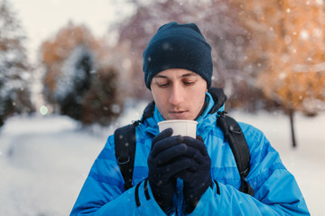 Fototapeta na wymiar Portrait of a man wearing bright blue winter sporty jacket and holding hot drink in disposable takeaway paper cup, outdoor shot