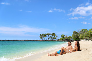 Fototapeta na wymiar Beach vacation relaxation. Happy couple relaxing sunbathing lying down on sand together tanning under the tropical sun in getaway travel destination. Young adults enjoying their holidays.