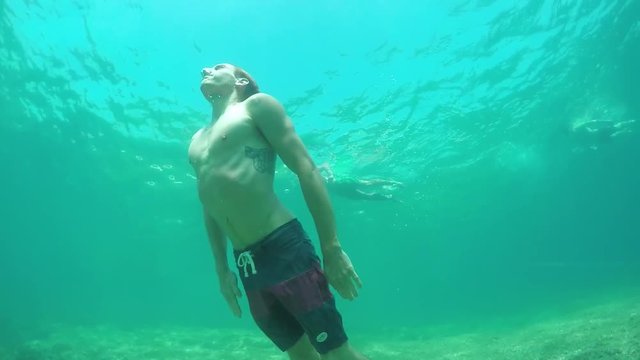SLOW MOTION UNDERWATER: Man swimming in the ocean, coming to the surface for air