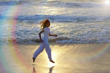 silhouette of woman running along the edge of sea on a sunset