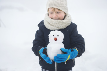 a happy boy in winter with a snowman in hands