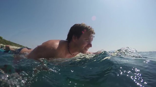SLOW MOTION OVER-UNDER: Pleased surfer man paddling on surf in open water ocean