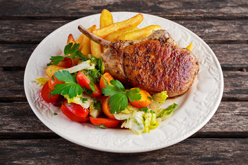 Grilled pork cutlet meat garnished with potato and salad on a wooden table.