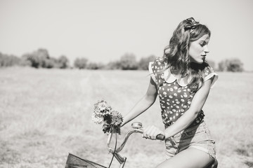 Young pinup woman cycling in fields under bright blue summer sky copy space image