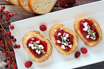 Crostini appetizers with cranberry sauce, brie, feta and rosemary overhead scene on a white plate