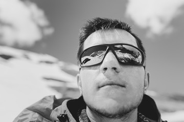 Black and white photograph of a young climber in sunglasses reflected snow capped mountains