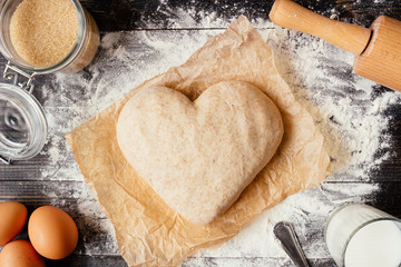 Cooking with love. Dough in heart shape top view. Baking ingredients on the wooden table