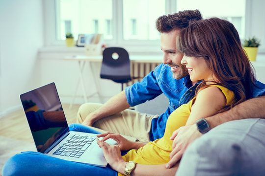 Happy young couple sitting on sofa at home with laptop