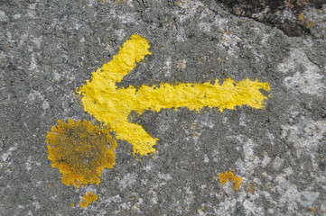 Gelber Pfeil auf Stein gemalt als Wegweiser am Jakobsweg in Spanien