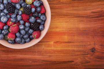 Fototapeta na wymiar Brown ceramic plate with berries on the left top corner of the wooden table with clipping path. Top view.