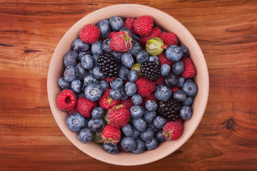 Brown ceramic plate with berries on the middle of the wooden table with clipping path. Top view.