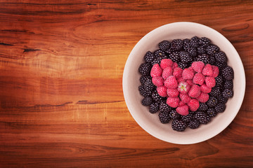 Ceramic plate with heart shaped berries on the left of the wooden table with clipping path. Top view.