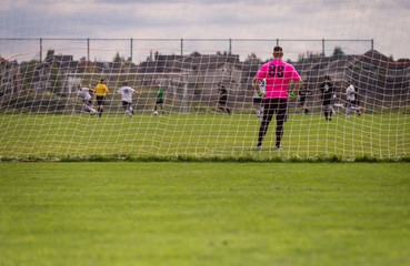 Male soccer goalie taking a break in the net with game in the background