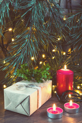 Christmas gift, light christmas candles and fir tree branch with lights decor on dark wooden background in vintage style. Coloring and processing photo