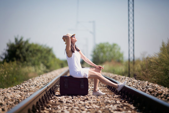 Woman on a railway sitting on a suitcase in retro style