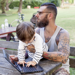 Obraz premium tattooed dad have fun with his son and laptop