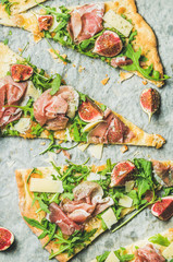 Naklejka na ściany i meble Pieces of fig, prosciutto, arugula and sage flatbread pizza on baking paper, top view, vertical composition