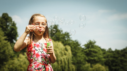 Little girl having fun blowing soap bubbles in park.