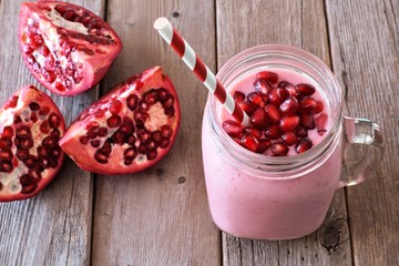 Pomegranate raspberry smoothie in a jar glass with pomegranate pieces, scene rustic wood
