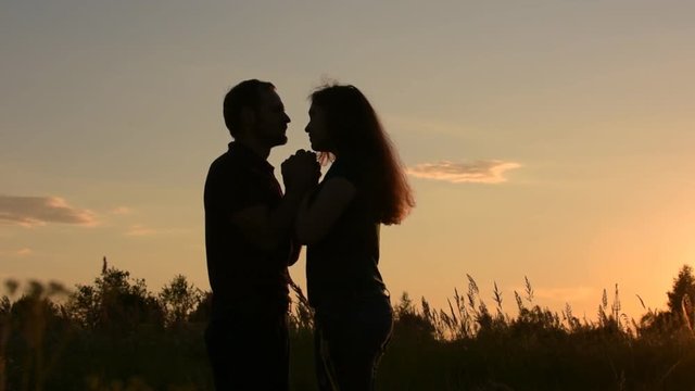 Beautiful couple in love holding hands show their feelings. Boyfriend kissing hands, and then the nose of his beloved. At sunset. Slow motion.