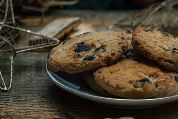 Beautiful concept. Close up Chocolate cookies on a white plate on a wooden background and tea. Nearby stands a Christmas tree, toys, garlands and Christmas toys.