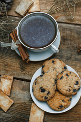 Beautiful concept. Chocolate cookies on a white plate on a wooden background and tea. Nearby stands a Christmas tree, toys, garlands and Christmas toys.