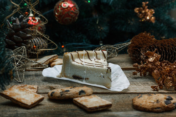 Beautiful homemade cake cheesecake on a white paper on the wooden background. Next chocolate chip cookies, Christmas gifts, Christmas tree, cones and toys. Conceived to celebrate the new year.