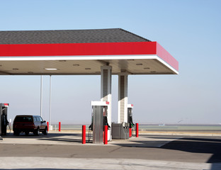 Gas station canopy on Interstate 5, central California. Gas pumps, one car, blue sky, and flat farmland. Horizontal.