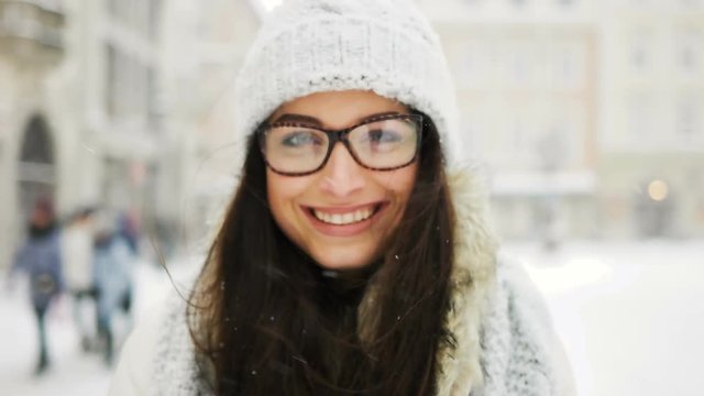 Street emotional portrait of young beautiful woman with glasses in city Model looking at camera. Lady wearing stylish classic winter knitted clothes. Christmas concept. Snowfall