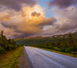 Obraz premium Highway road for cars in norwegian mountains. Dramatic sunset clouds and mountain landscape, driving asphalt, trip from Oslo to Bergen, Norway, Scandinavia. Rural country way in green mountains valley