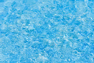 Blue and bright water surface in swimming pool with sun reflection