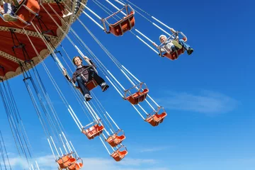 Fotobehang Amusementspark Moeder met de zesjarige zoon rijdt in een attractie op een schommel tegen de blauwe lucht in een pretpark