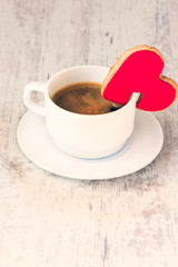 Valentines day background. Top view of a heart shaped cookie with red icing and a cup of coffee over a white wood rustic background. Love concept. Copy space.