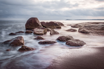 Obraz premium Sunrise over the sea rocks on the beach. Smooth waters, long exposure effect. Seascape in beautiful blue and purple colors.