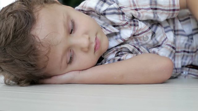 Portrait of sad little boy lying on floor at home at the day time 