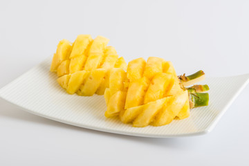 Small pineapple slices and leaves in plate on white background