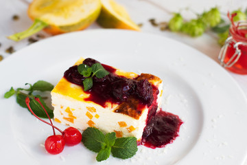 Close up of cheesecake with cherry and jam on white plate. Sweet dessert serving, pumpkin and hop on blurred foreground. Autumn menu, restaurant cuisine, pastry concept