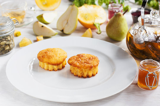 Tasty muffins on white plate, pear and tea on background. View on kitchen table with sweet cupcakes and beverage, free space for text
