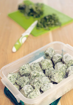 Frozen vegetables and cutting board and plastic containet with frozen herbal cubes