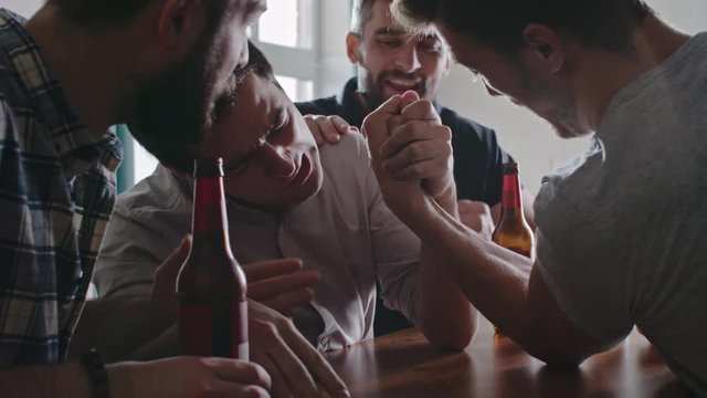 Asian man arm wrestling his friend at party while their mates cheering and laughing
