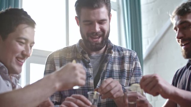 Male friends taking shots of vodka with lemon and then wincing