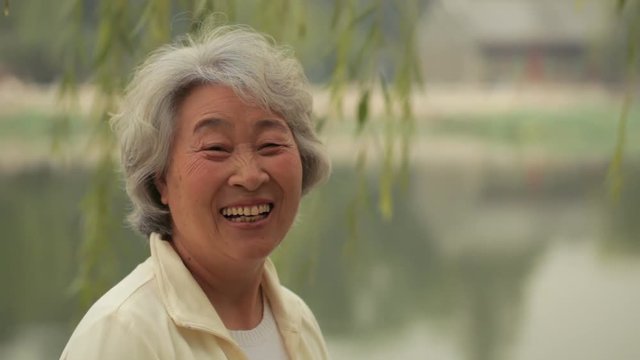 MS Senior woman looking at camera and smiling by the lake / China