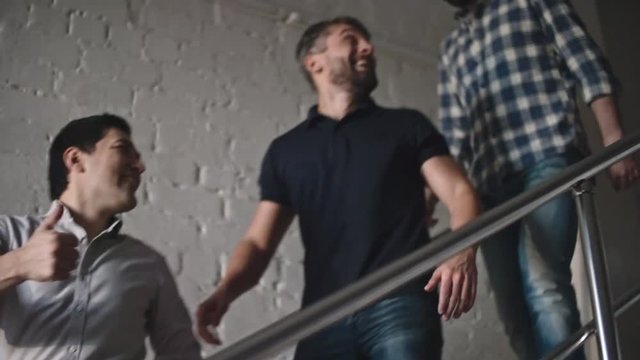 Handheld shot of male friends walking down stairs chatting and laughing