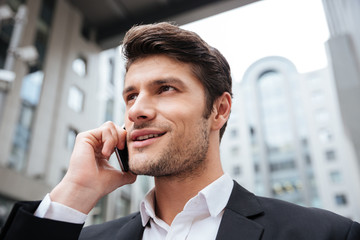 Cheerful attractive young businessman talking on cell phone outdoors