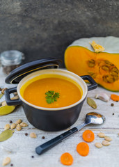 Creamy pumpkin soup with herbs and vegetables in a pot on a wooden table. Vegetarian food.
