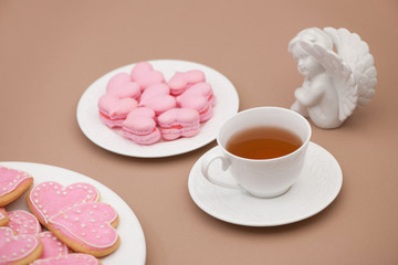 Fototapeta na wymiar pink cookies in the shape of hearts on a plate with a cup of tea and an angel on Valentine's Day