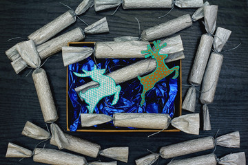 Сandy in a silver wrapper on a black wood background. Blue wrapping paper and kraft box. Christmas decorations in the form of a deer. Top view, flat lay
